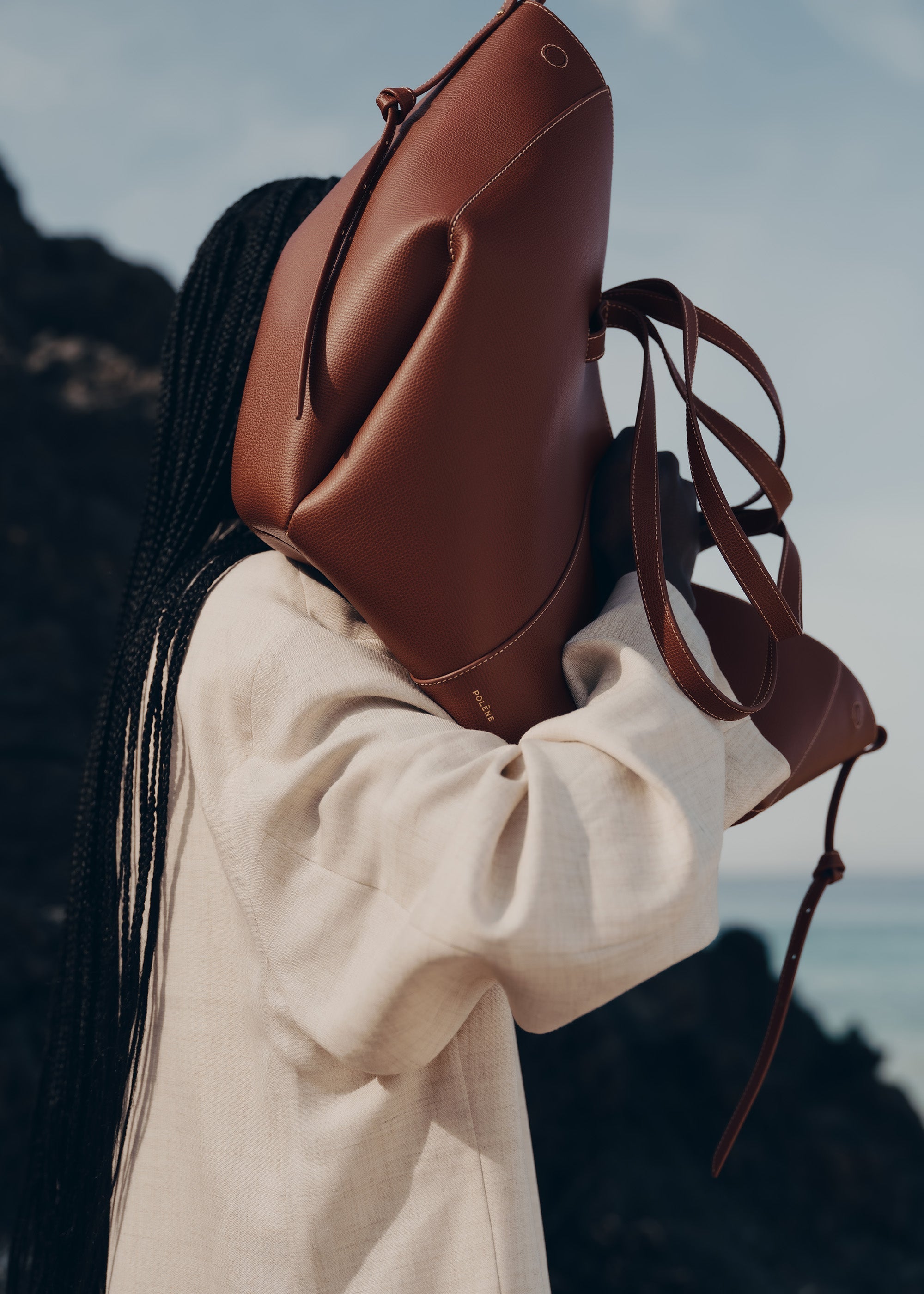 Bolso de mano Polène Cyme en piel granulada color coñac, con diseño elegante y detalles en la superficie de la cartera.
