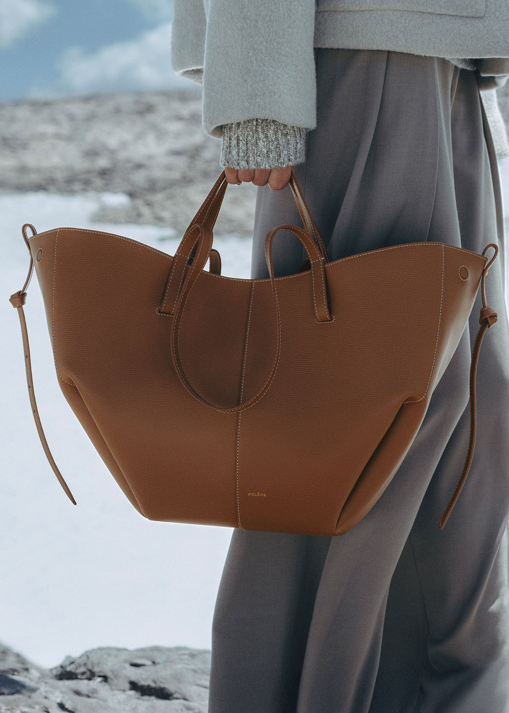Bolso de mano Polène Cyme en piel de camello granulado, con diseño elegante y detalles en la superficie de piel texturizada.