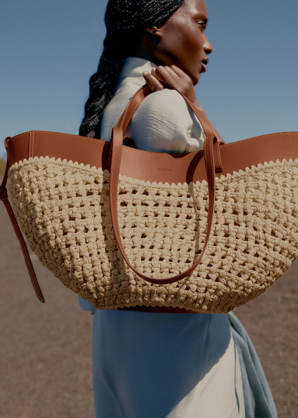 Bolso de mano Polène Cyme en rafia con asa larga y diseño elegante, visible en imagen.
