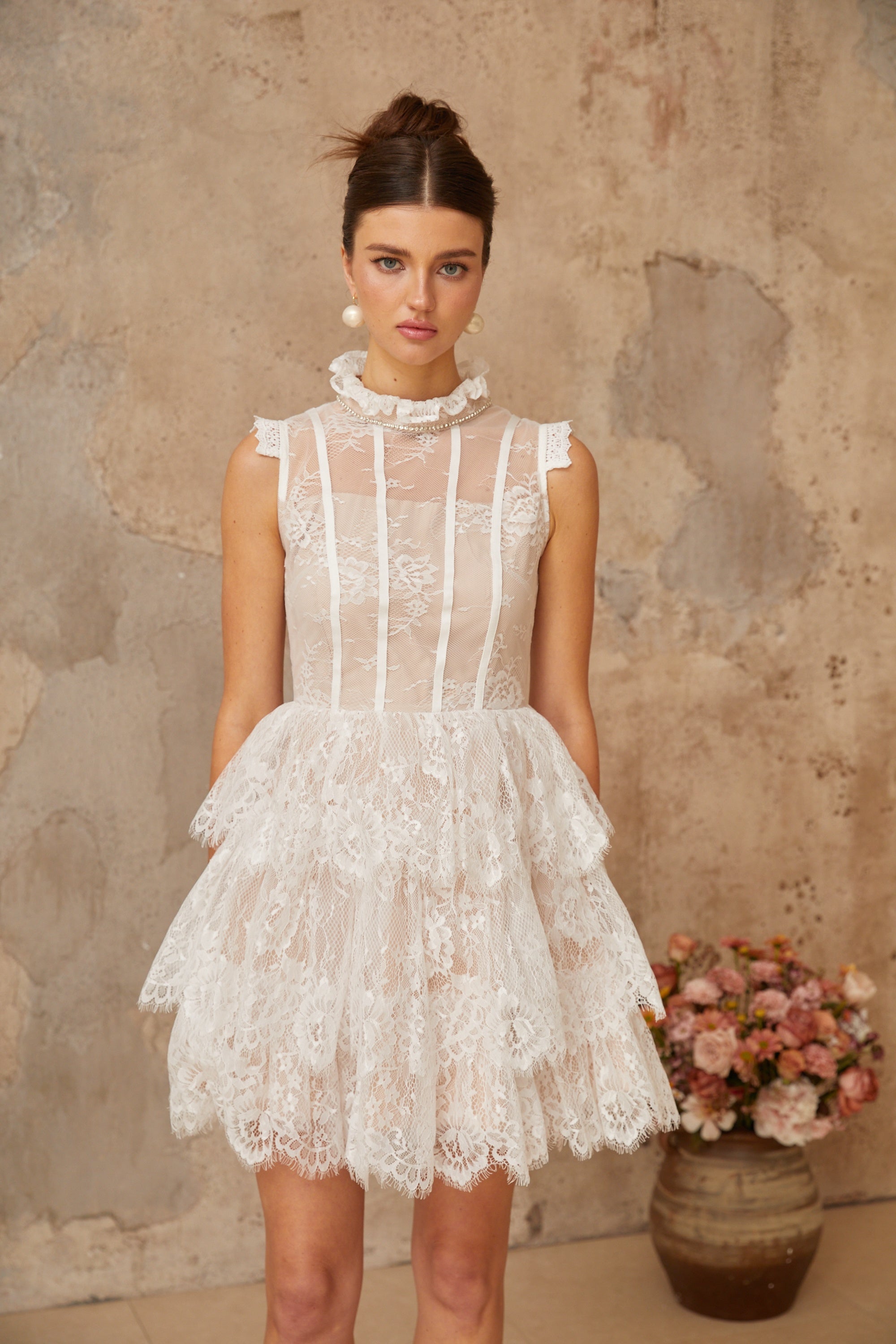 Vestido mini blanco con encaje floral y detalles adornados, con varias capas y diseño elegante.