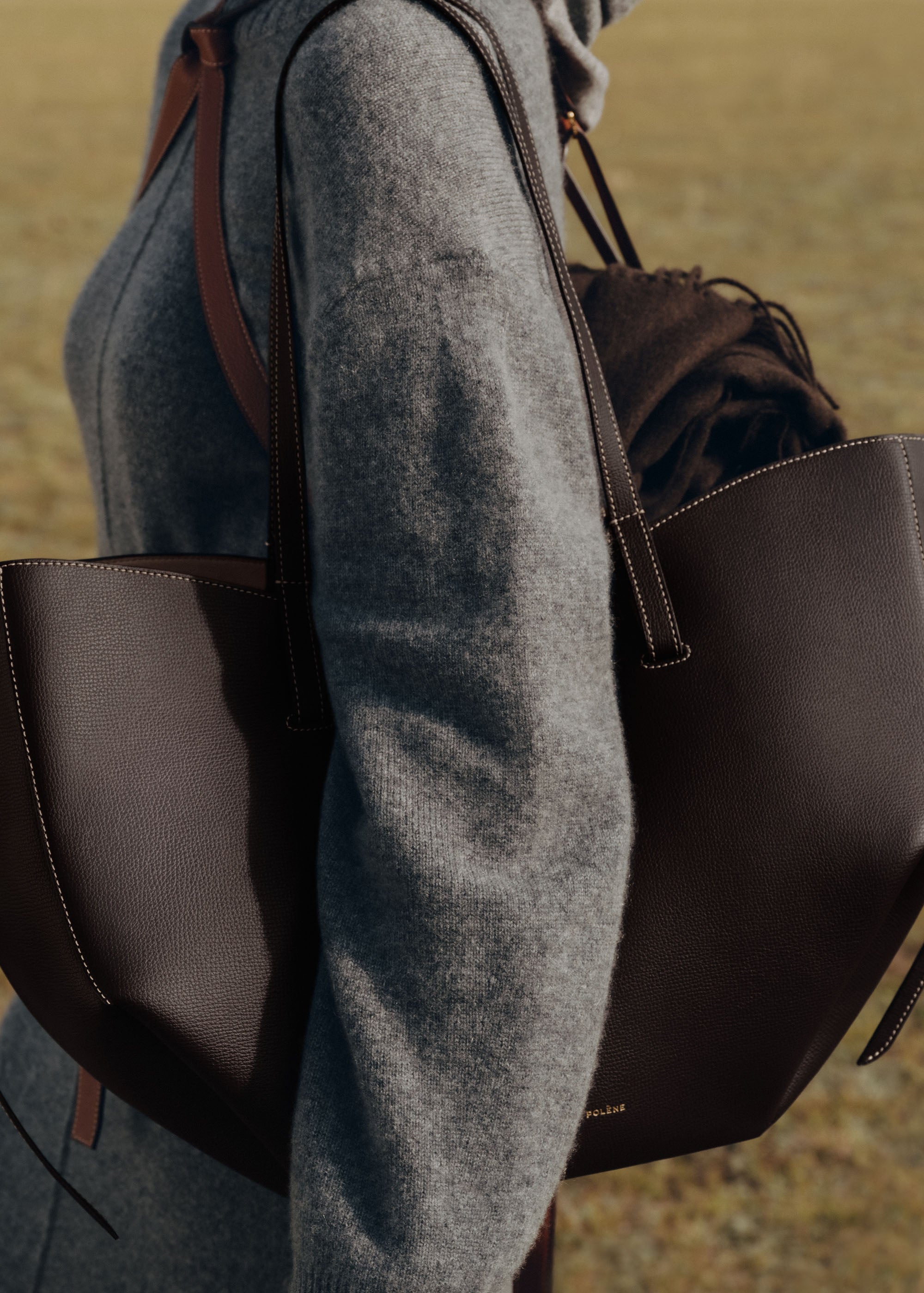 Bolso de mano Polène Cyme en piel de ébano granulado con detalles de costura y diseño elegante.