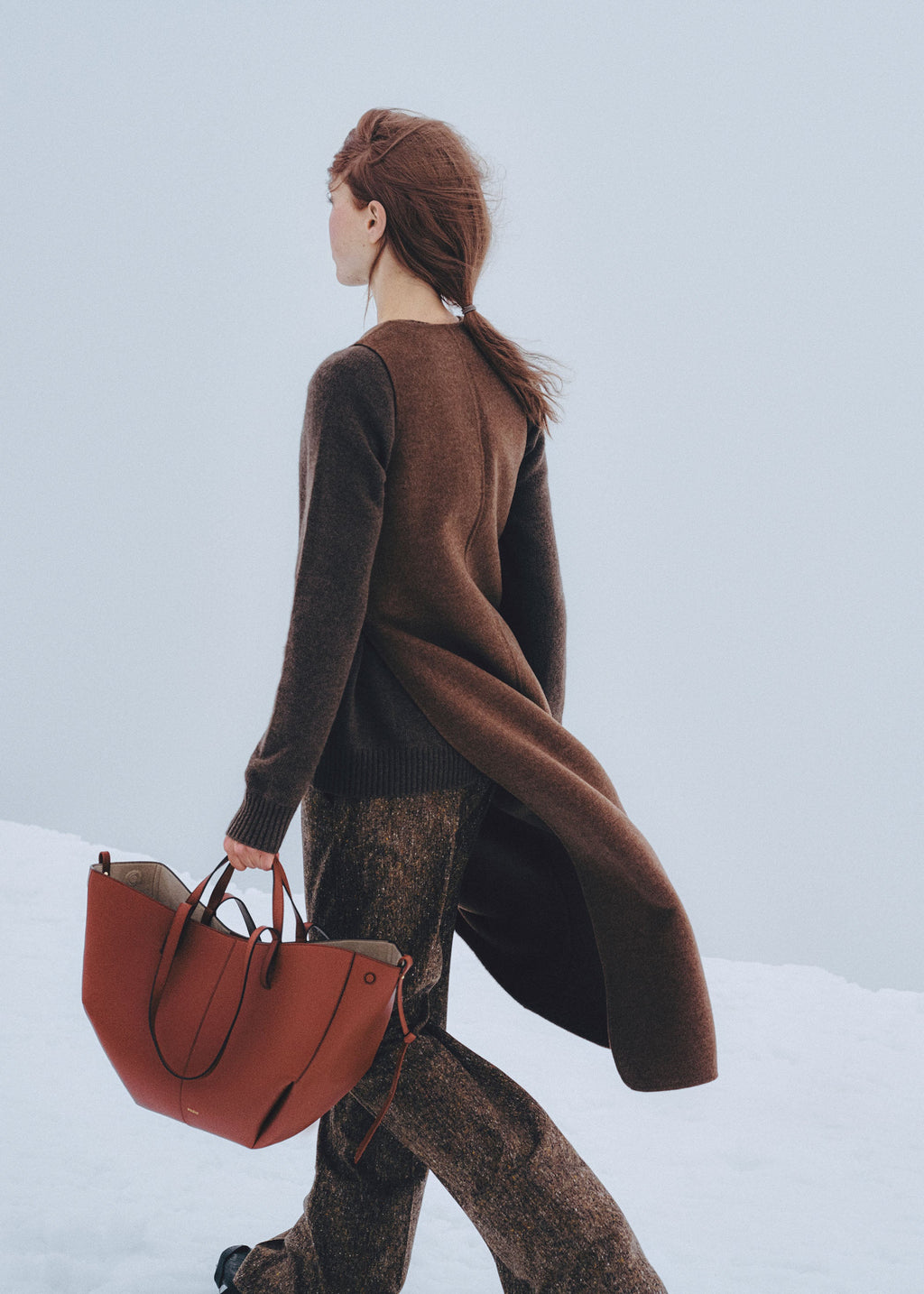 Bolso de mano Polène Cyme en arcilla roja con textura granulada, detalle de la superficie y diseño elegante.
